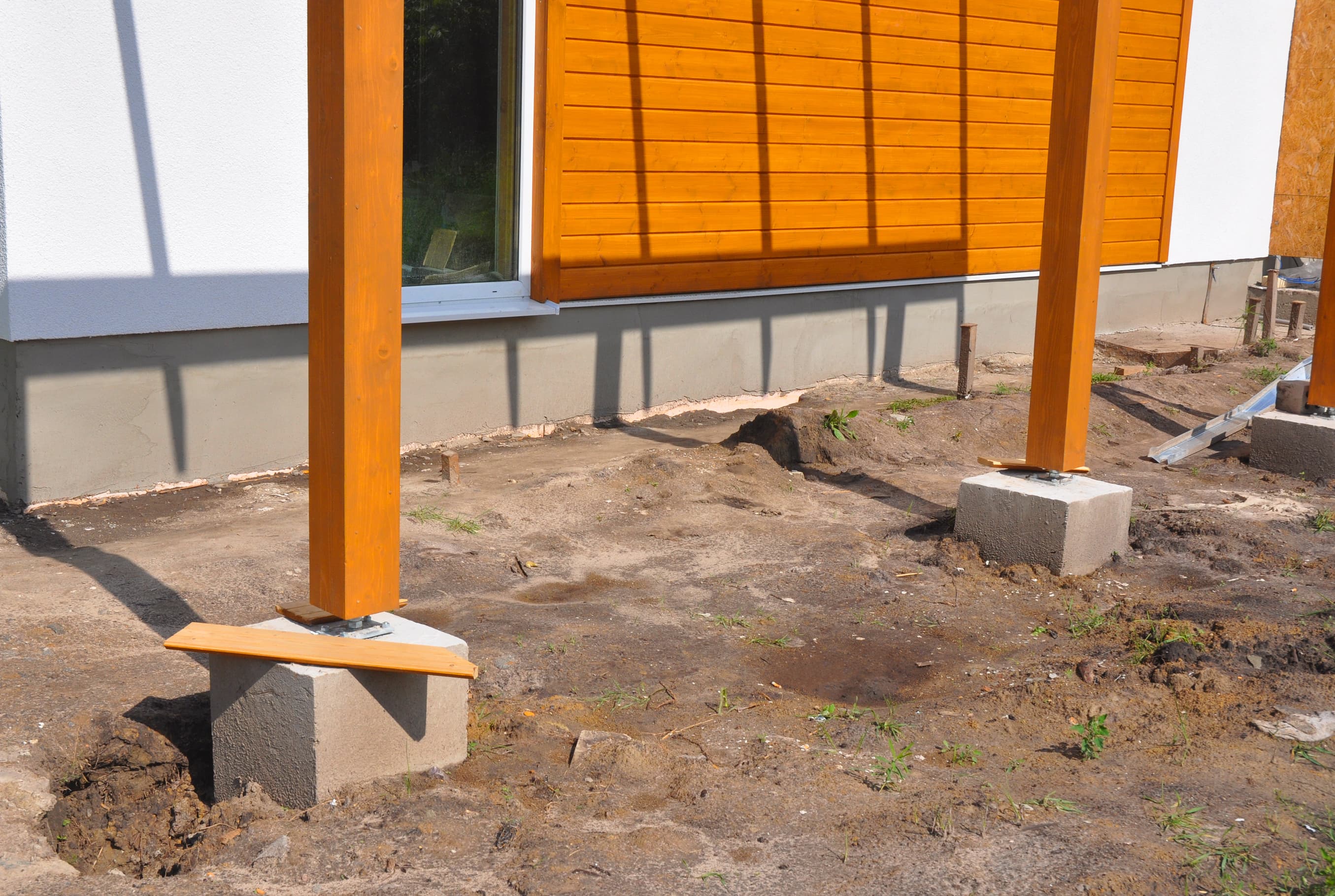 Holzpfosten vor einer Hauswand sind auf dem Fundament der Terrassenüberdachung verschraubt.