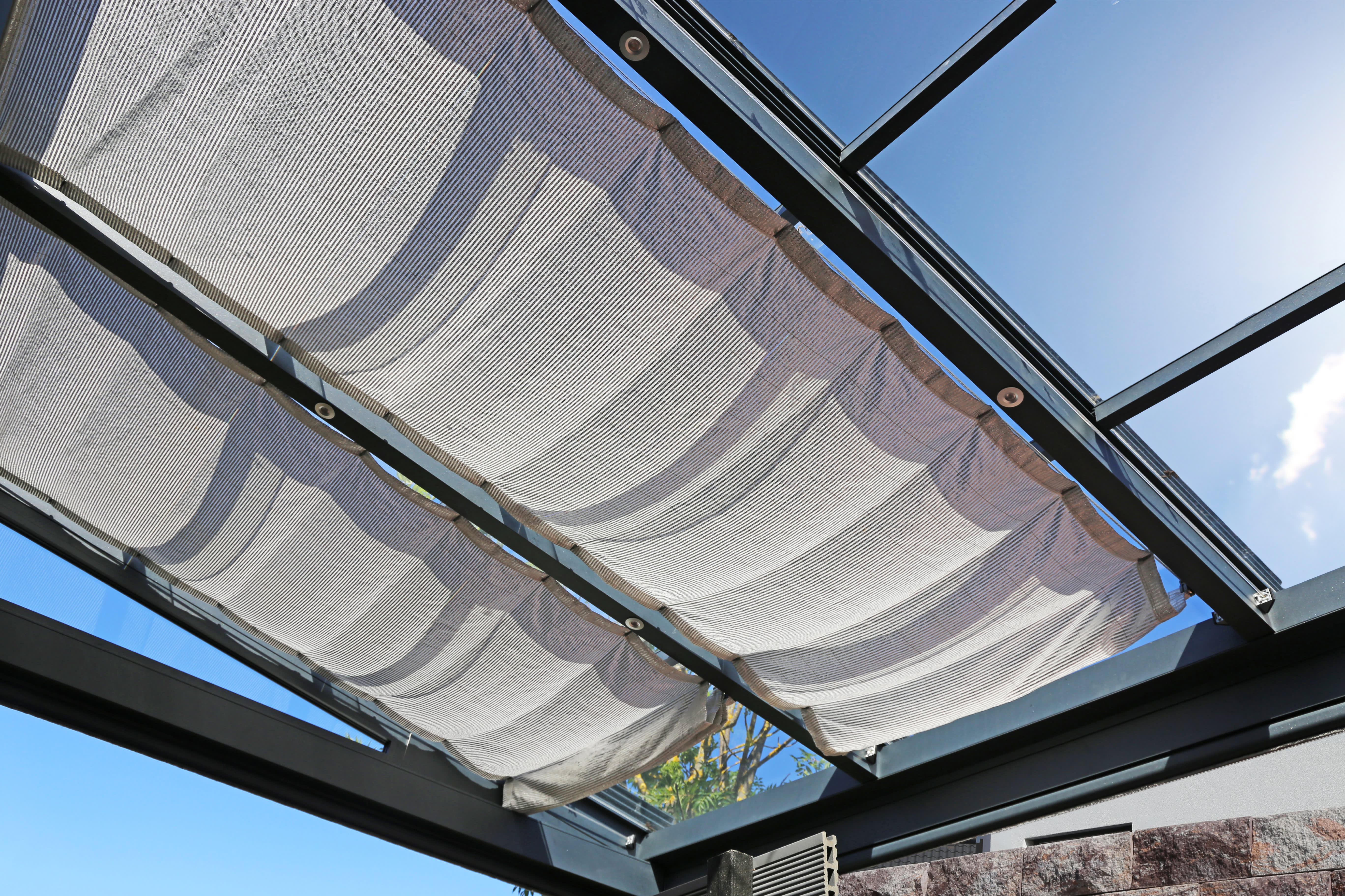 Zwei Sonnensegel aus Leinenstoff an einer Terrassenüberdachung