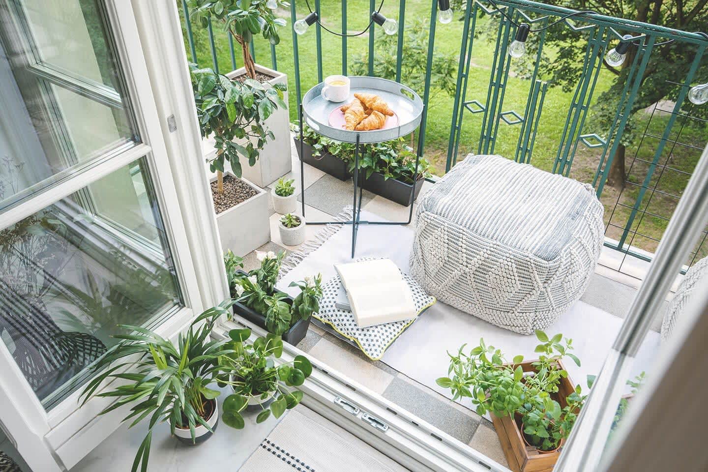 Kleiner Balkon mit Sitzgelegenheit, Tisch und Topfpflanzen bei geöffneter Balkontür von innen fotografiert