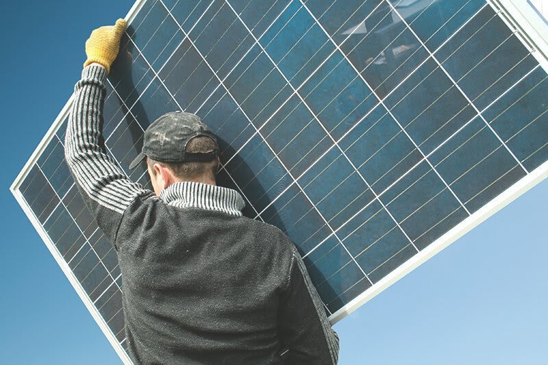 Solarmodul wird von einem Handwerker getragen.