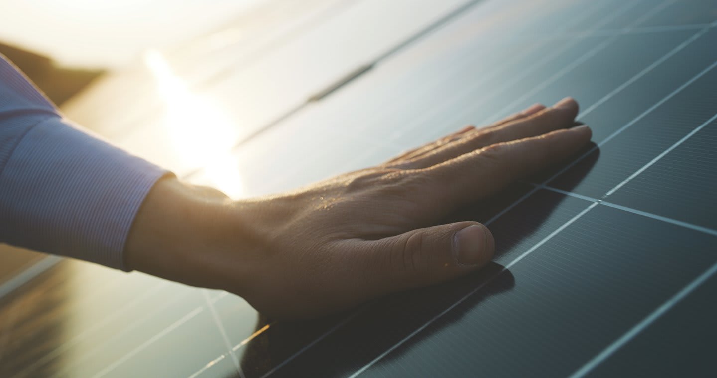 Eine Hand auf einem Solarpanel, im Hintergrund spiegelt sich die Sonne auf weiteren Solarzellen