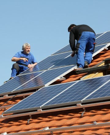 zwei Solarteure montieren Photovoltaik auf einem Ziegeldach