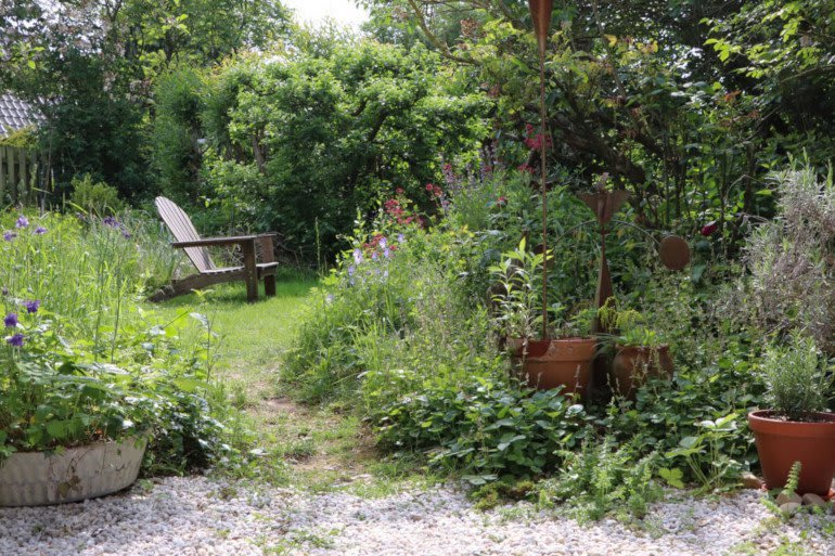 Wilder, bewachsener Garten mit verschiedenen Pflanzen, Pflanzkübeln und einem Gartenstuhl auf der Wiese 
