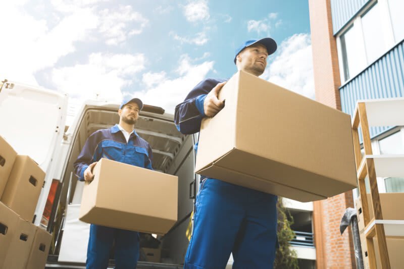 Mitarbeiter einer Umzugsfirma tragen Kisten aus einem Transporter in eine neue Wohnung