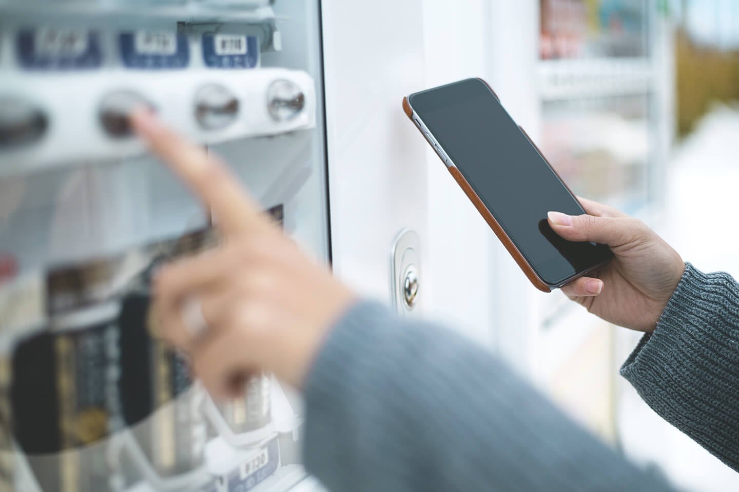 Hand bedient Getränkeautomat und hält dabei ein Handy in der Hand