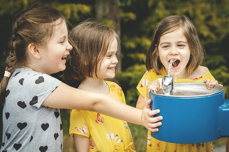 Kinder stehen an Trinkbrunnen und trinken