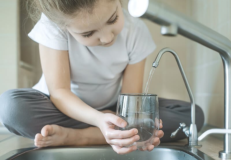 Kind füllt Wasserglas an Wasserhahn auf