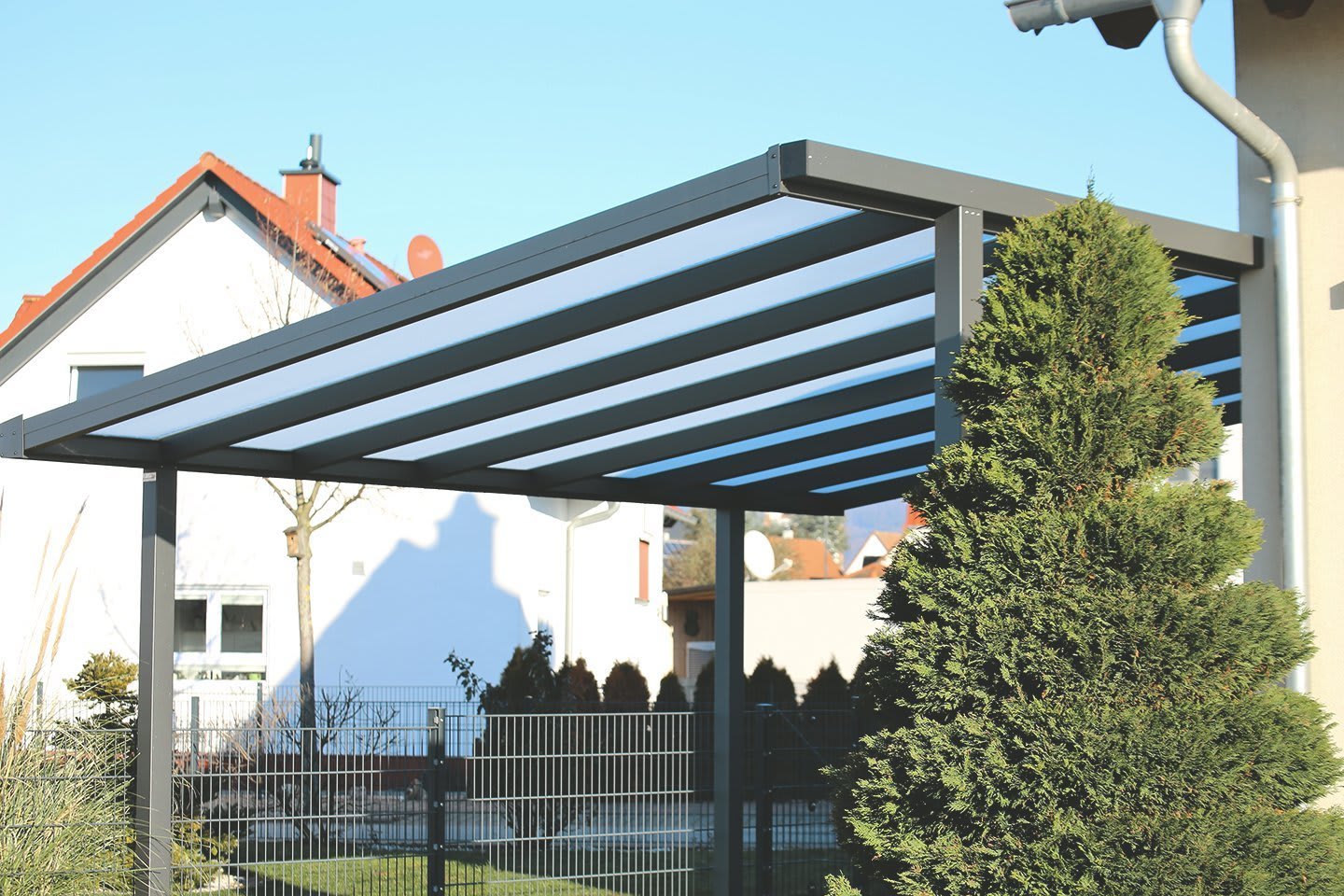 Carport aus Metall mit transparentem Dach neben Wohnhaus