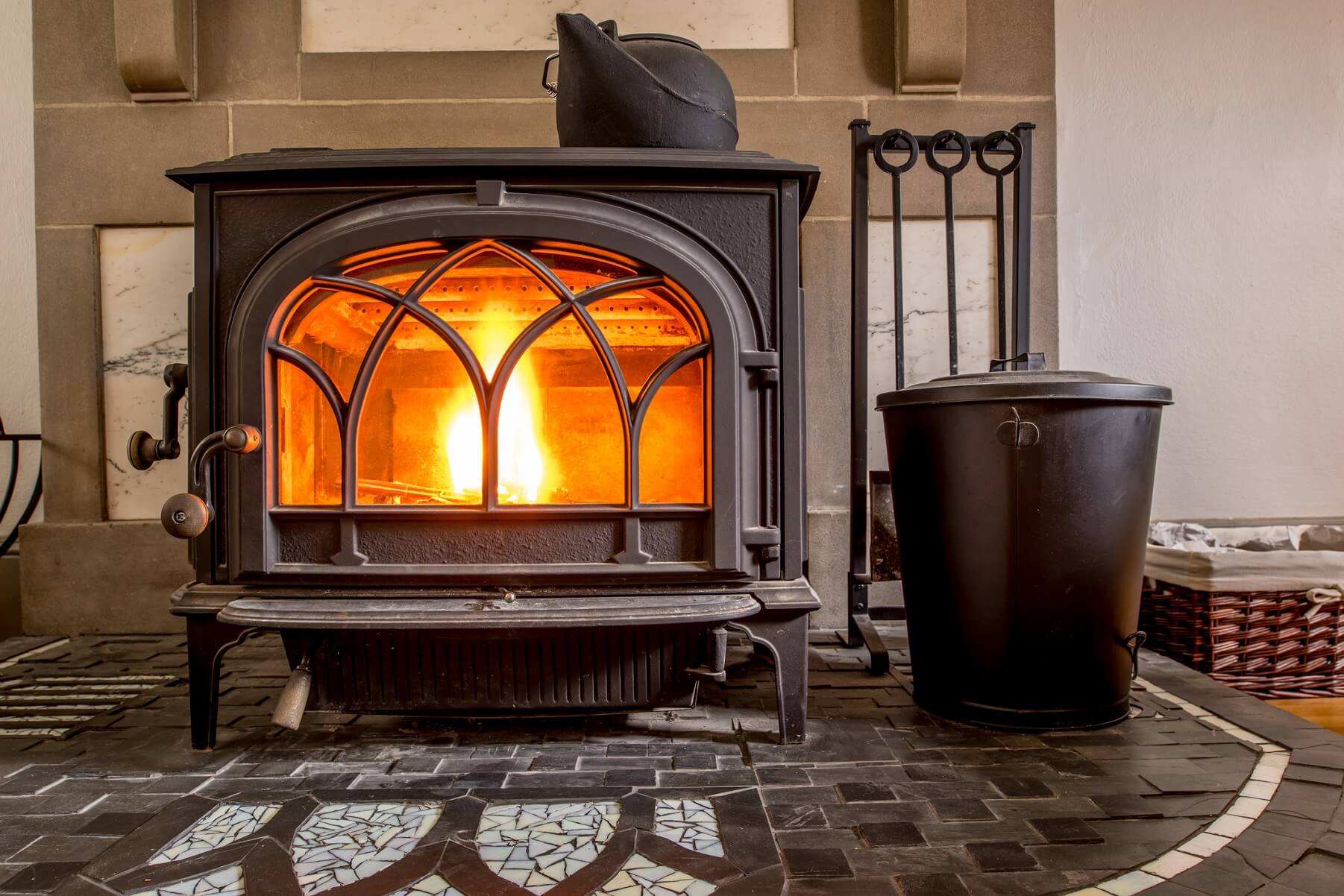 Moderner brennender Kaminofen aus Gusseisen im Wohnraum mit gusseisernem Teekessel zur Luftbefeuchtung oben auf dem Ofen