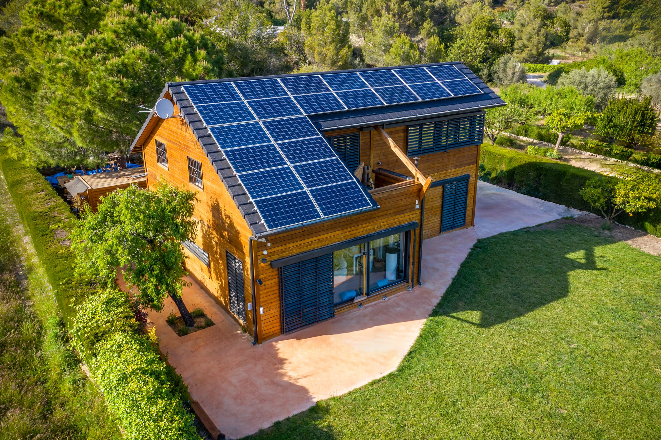 Photovoltaik-Paneele auf einem Holzhausdach umringt von grünem Garten